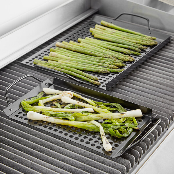 Two Outset non-stick grill trays with asparagus and green onions cooking on a grill.