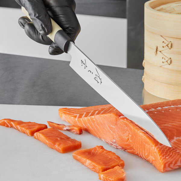 A person using a Mercer Culinary left-handed Sashimi knife to cut a piece of salmon on a counter.