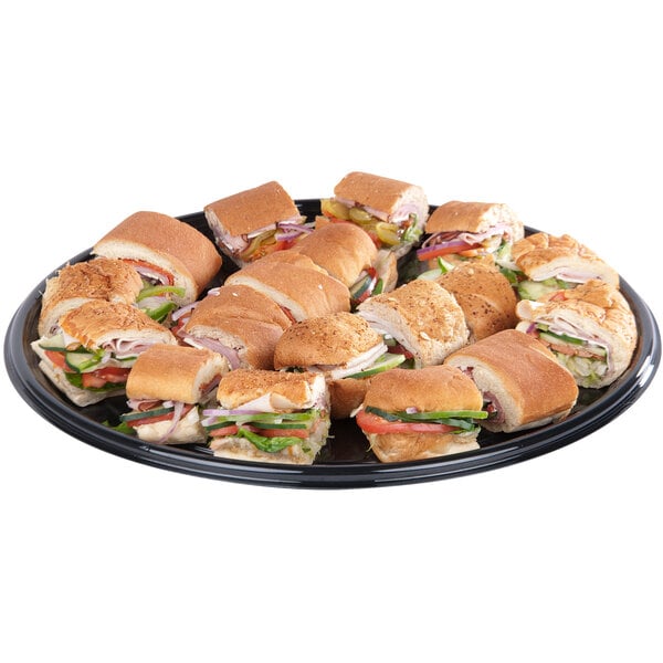 A Sabert black round catering tray filled with sandwiches on a table.