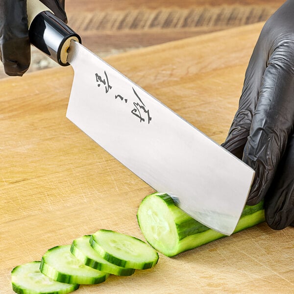 A person in black gloves cutting a cucumber in half with a Mercer Culinary Nakiri Knife.