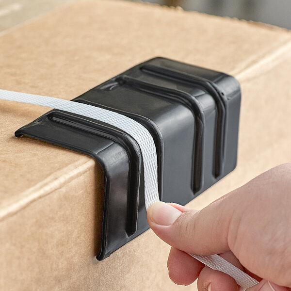 A person's hand holding a black box of PAC Strapping Products black plastic strapping edge protectors.