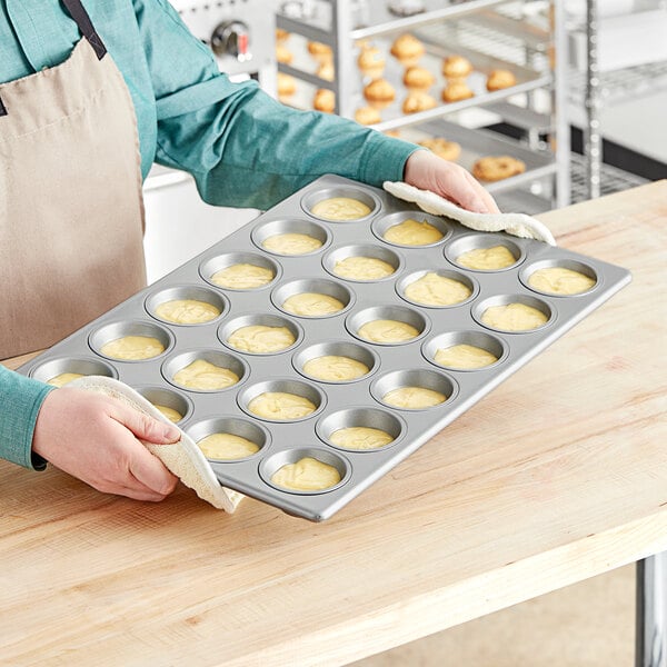 A person holding a Baker's Mark muffin and cupcake pan with muffins in it.