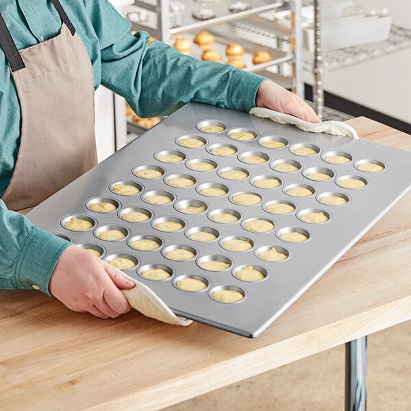 A person holding a Baker's Mark aluminized steel mini muffin pan filled with muffins.