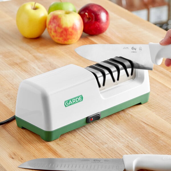 A person using a Garde electric knife sharpener to cut a green apple.