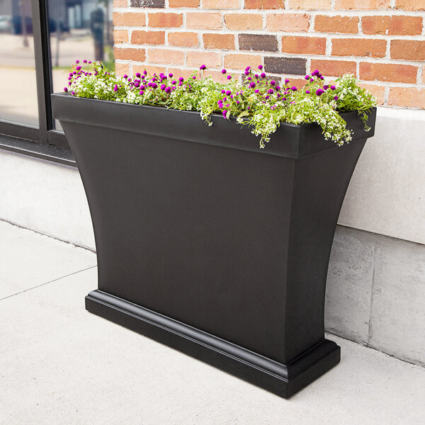 A black rectangular Mayne trough planter with flowers in it.