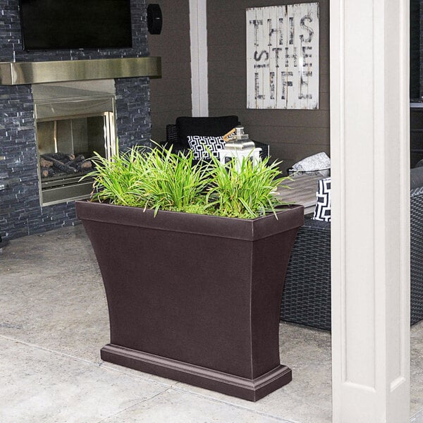 A Mayne Bordeaux espresso planter with grass in it on an outdoor patio.