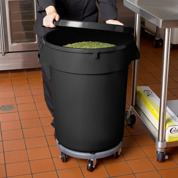 A woman holding a large black 32 gallon mobile ingredient storage bin full of green beans.