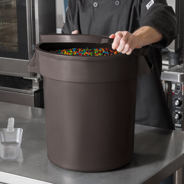 A man in a chef's uniform pouring a brown ingredient storage container full of candy.