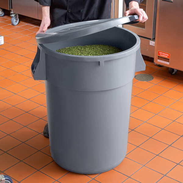 A woman holding a grey round ingredient storage bin filled with green beans.