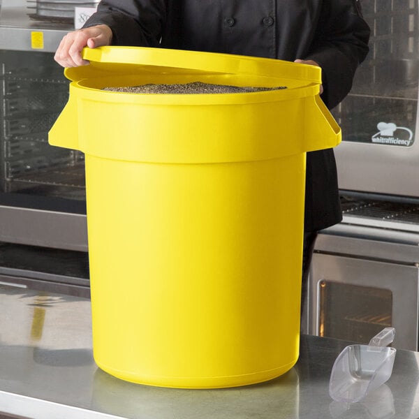 A woman in a black chef's uniform holding a yellow round ingredient storage bin with a lid.