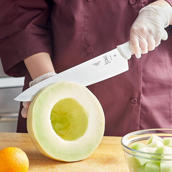 A hand holding a Mercer Culinary Ultimate White&#174; Chef Knife cutting a melon.