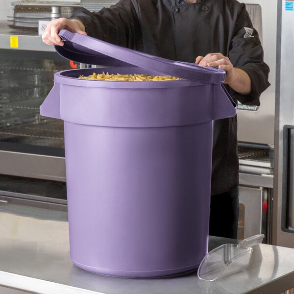 A man in a chef's uniform holding a purple round ingredient storage bin full of noodles.