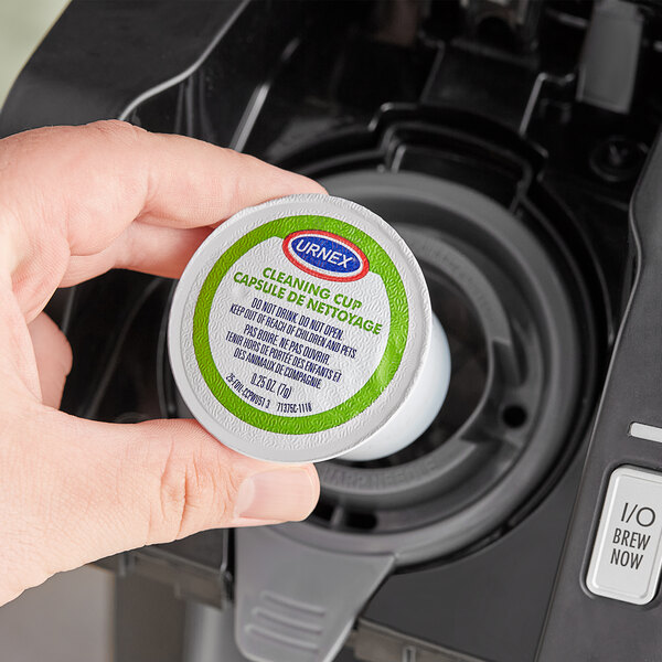 A hand holding a round container of Urnex K-Cup Single Cup Coffee Brewer Cleaning Cups.