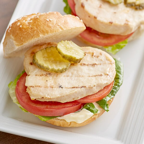A white plate with a chicken sandwich made with Brakebush Easy Gourmet Classic Boneless Skinless Grilled Chicken Breast Fillet.