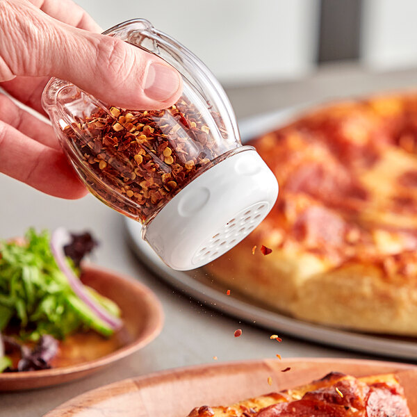A person using a Tablecraft clear plastic swirl pepper shaker to pour pepper onto a plate of food.