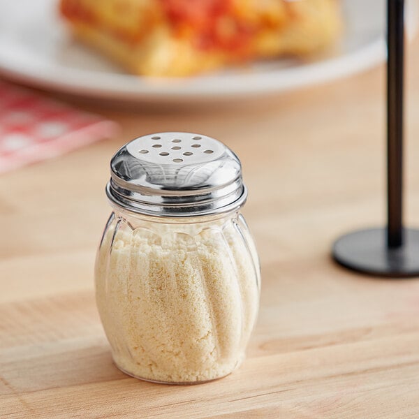 A Tablecraft clear plastic salt shaker with a chrome plated lid on a table in a pizza parlor.