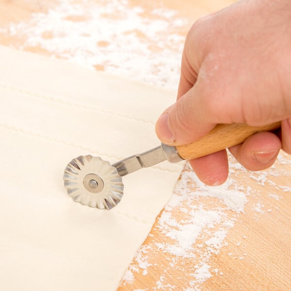 A hand uses an Ateco stainless steel pastry cutter with a wood handle to cut dough.