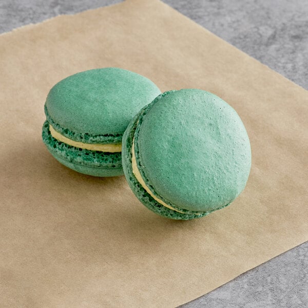 Two green Macaron Centrale matcha macarons on brown paper.