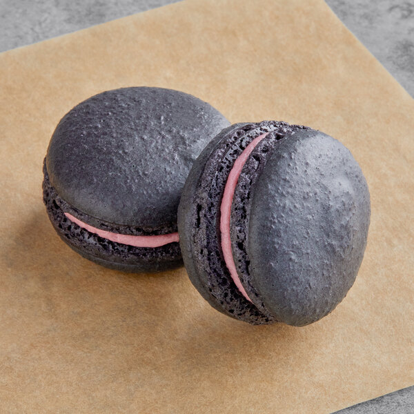Two black Macaron Centrale macarons with pink filling on a piece of paper.
