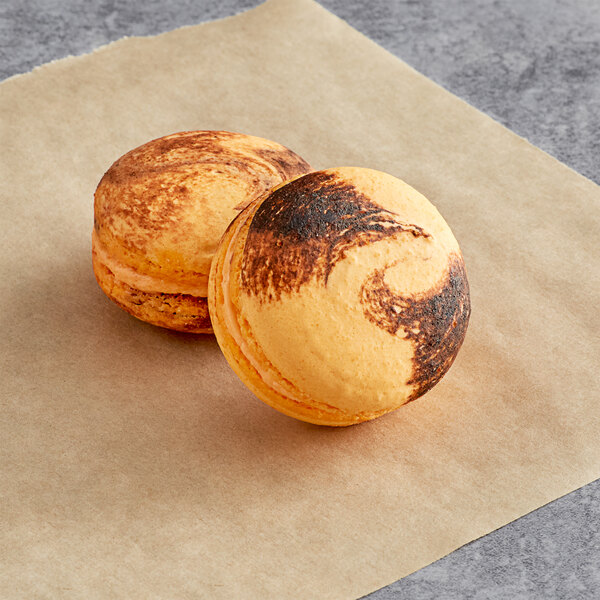 Two Macaron Centrale Thai Tea macarons on a piece of paper with brown and orange swirls.