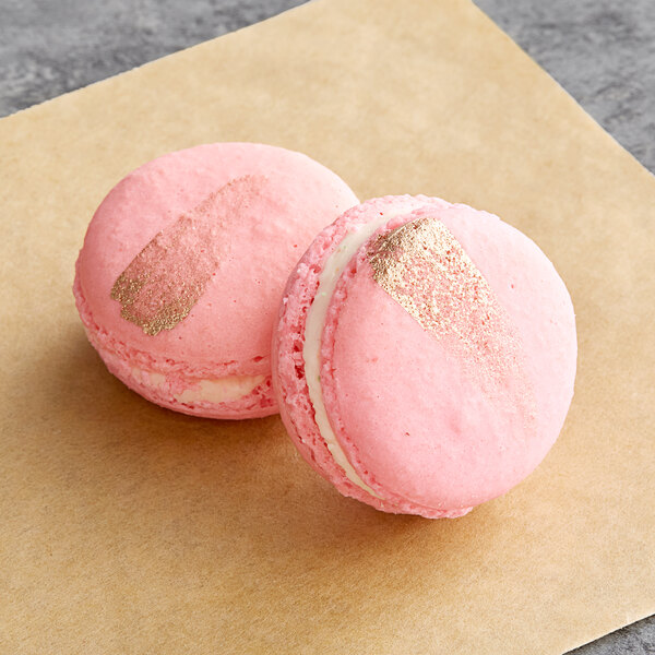 Two pink Macaron Centrale macarons with gold foil on a brown surface.
