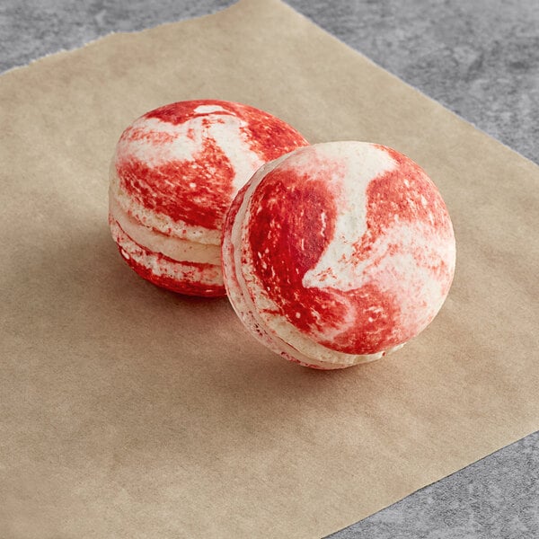 Two Macaron Centrale strawberry cheesecake macarons with red and white shells on a piece of paper.