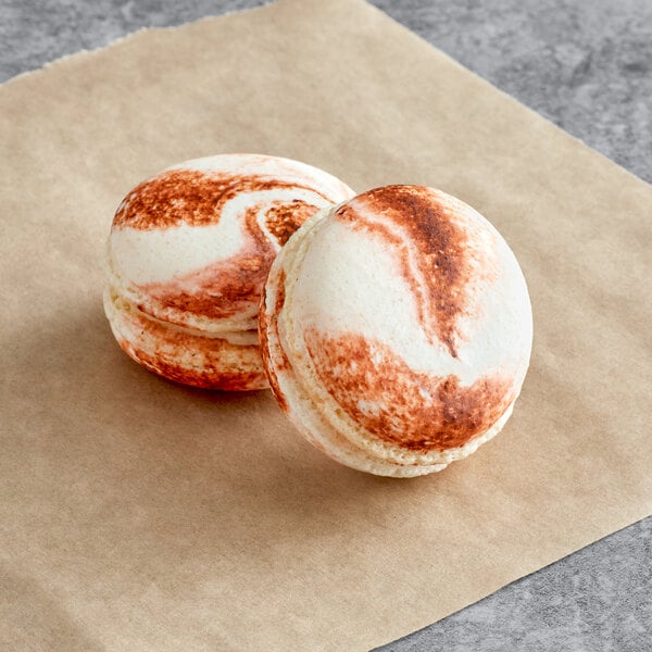 Two Macarons with brown and white icing on a paper.