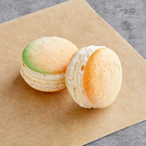 Two Macaron Centrale pineapple macarons on a brown paper with white and green frosting.