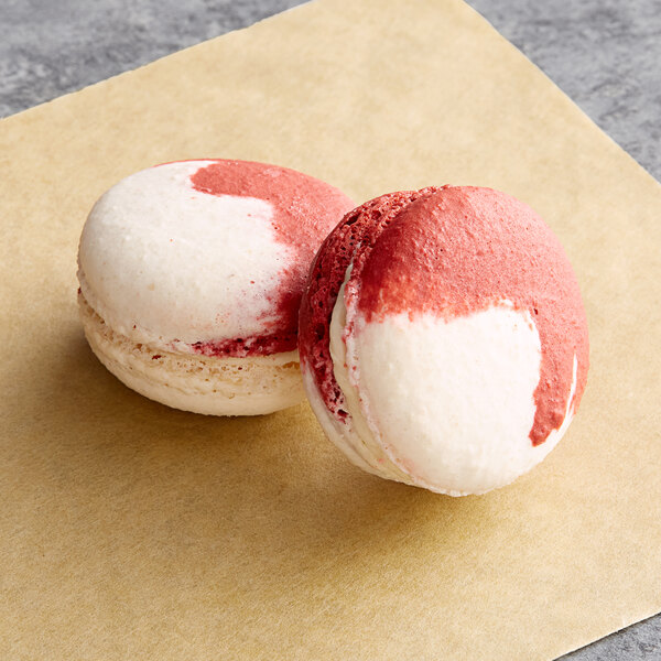 Two Macaron Centrale peppermint macarons with pink and white icing on a brown paper.