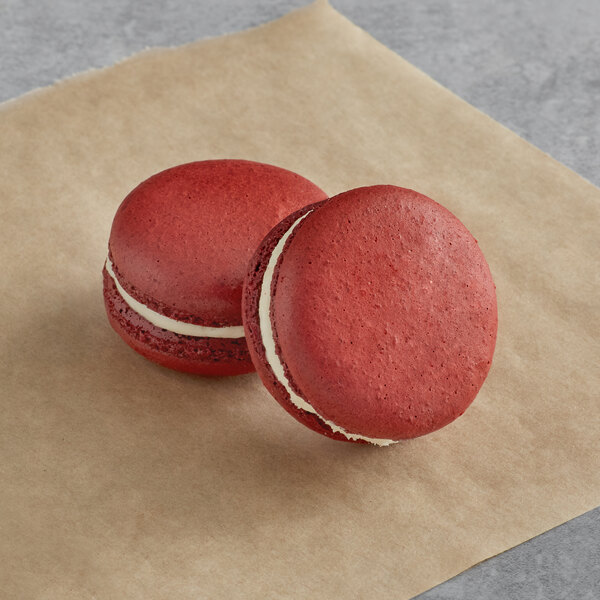 Two red Macaron Centrale red velvet macarons on a brown surface.