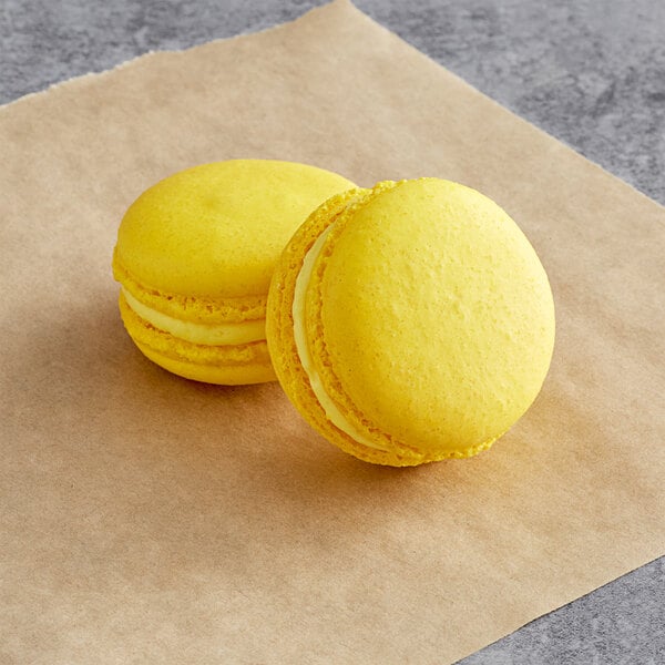 Two yellow lemon macarons on a piece of brown paper.