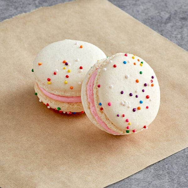 Two Macaron Centrale birthday cake macarons with white cookies and sprinkles on top.