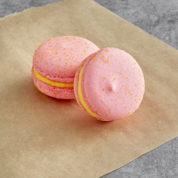 Two pink and yellow Macaron Centrale macarons on a brown paper.