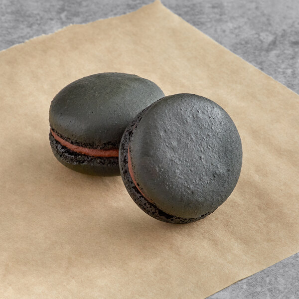 Two black Macaron Centrale espresso macarons on brown paper.