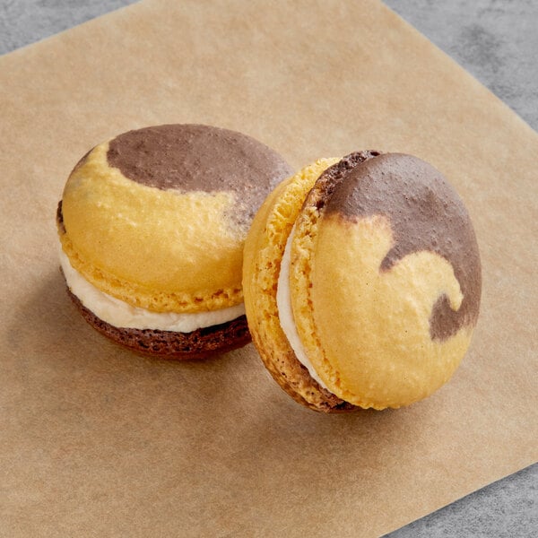 A close-up of two Macaron Centrale Dulce de Leche macarons on a paper.