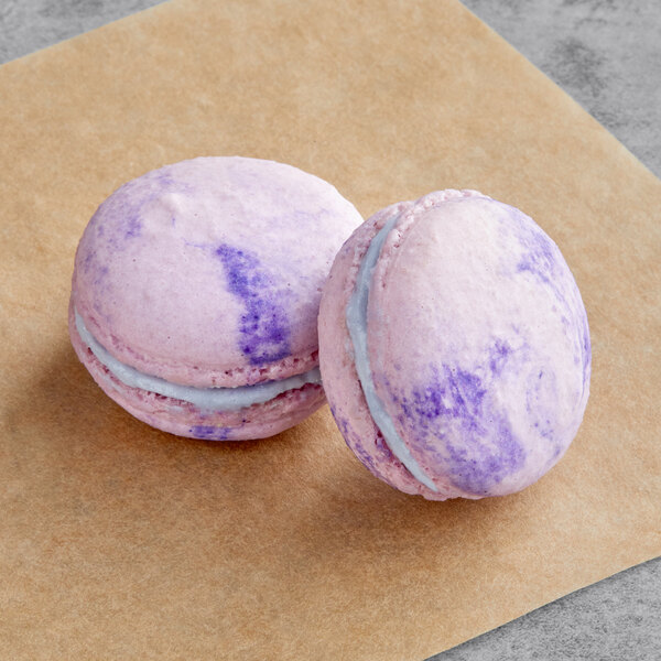 Two butterfly pea flower macarons, one pink and one purple, on a brown paper.