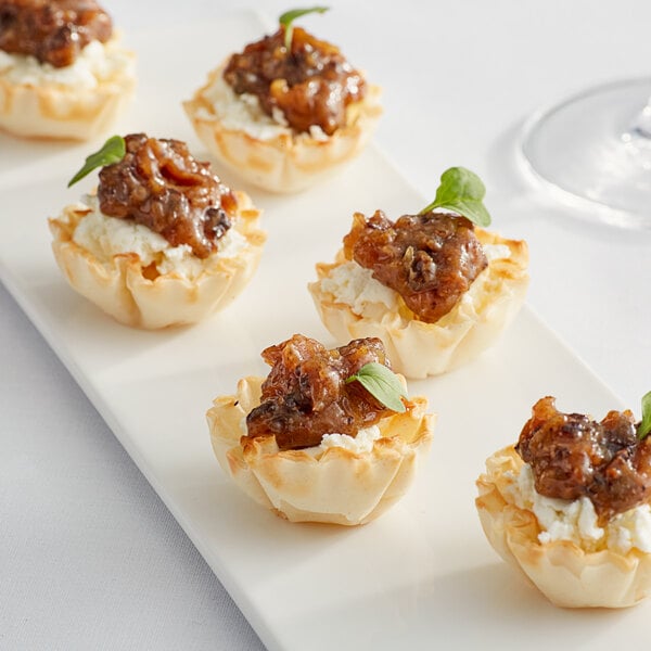 A white plate of small appetizers topped with TBJ Gourmet Classic Uncured Bacon Jam.