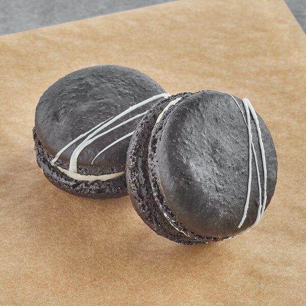 Two black Macarons with white icing on a brown surface.