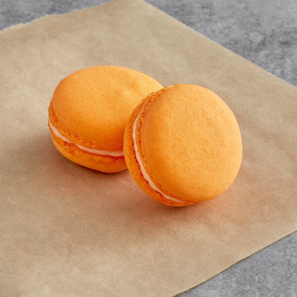 Two orange Macaron Centrale cookies with white filling on a brown surface.