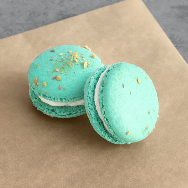 Two green pistachio macarons on brown paper.