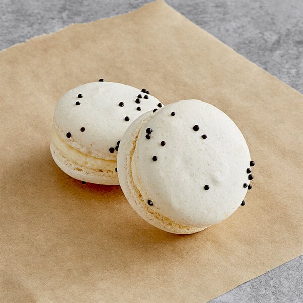 Two Cookies and Cream Macarons with black dots on top.