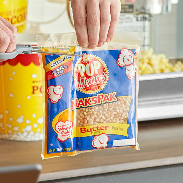 A person holding a Pop Weaver All-In-One Naks Pak popcorn bag in front of a popcorn machine.