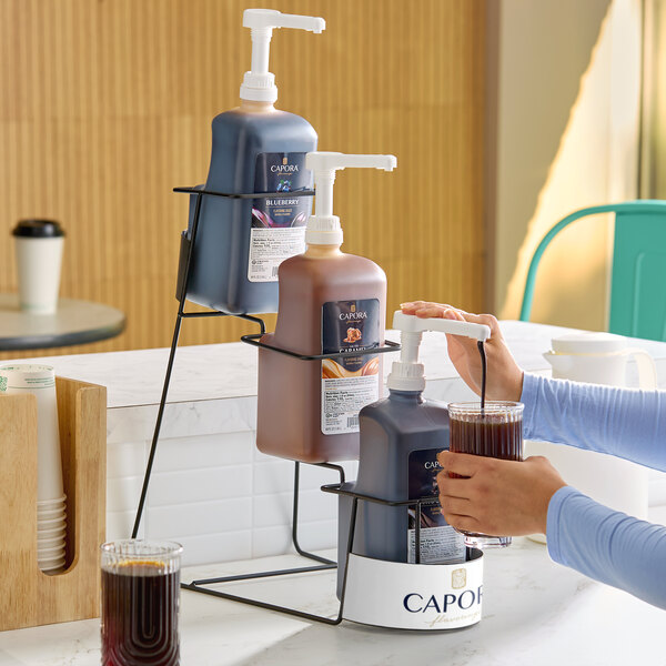 A three-tier metal rack holding three large pump bottles of flavoring sauce for beverages.