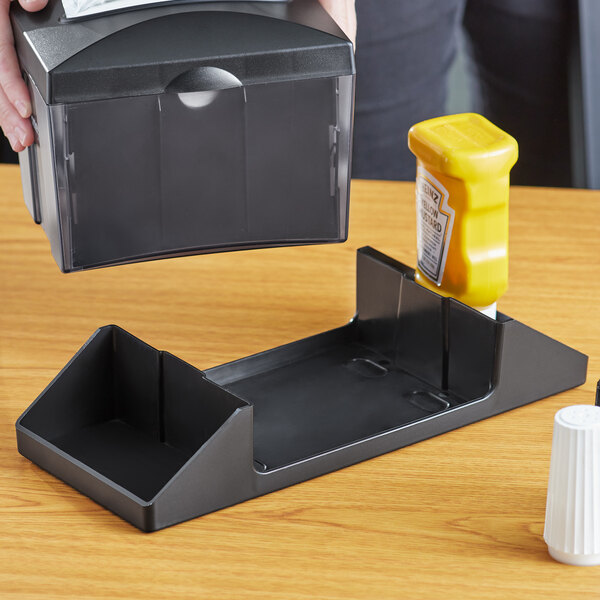 A black plastic condiment caddy with a yellow bottle of mustard on a table.