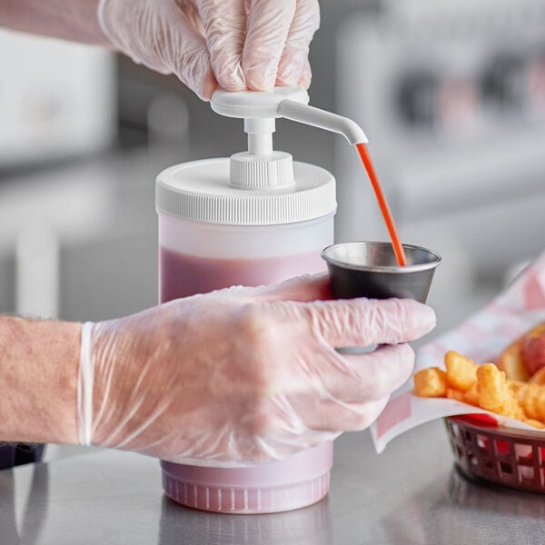 A person in a pink glove using a Choice plastic pump to pour sauce into a container on a counter.