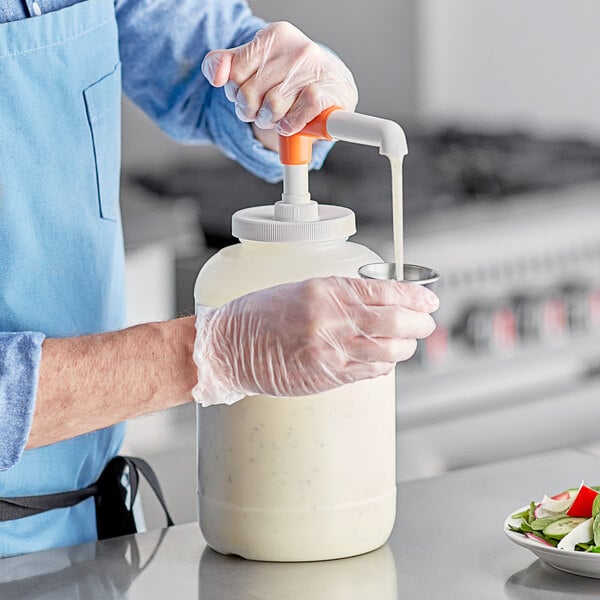 A person in a blue apron using a Choice condiment pump to pour white liquid into a container.