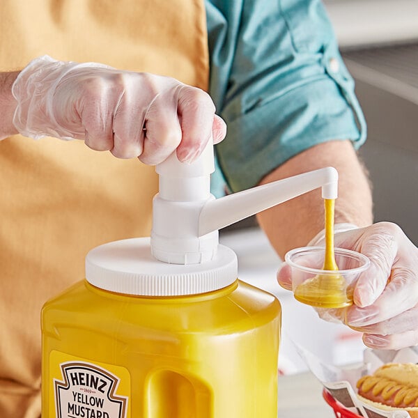A hand using a white Choice condiment pump to pour yellow mustard into a plastic container.