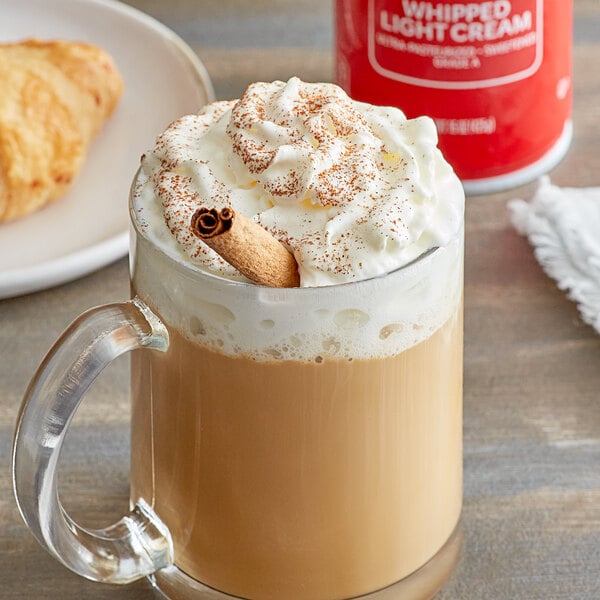 A glass mug of coffee with Reddi-Wip whipped cream and a cinnamon stick.