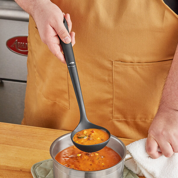 A person using an OXO Good Grips ladle to pour soup into a pot.