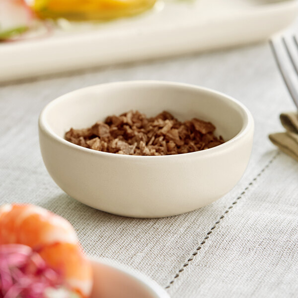 A fog white Acopa Pangea ramekin filled with brown food on a table.